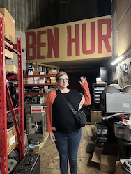 A woman holds up a hand under a Ben Hur poster