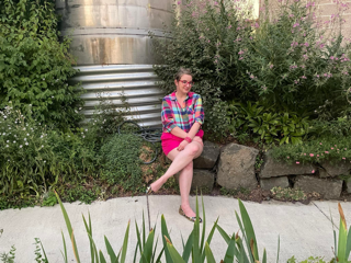 A woman sits in front of many plants with her legs crossed