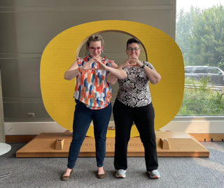 Two women link arms and make an O with their hands