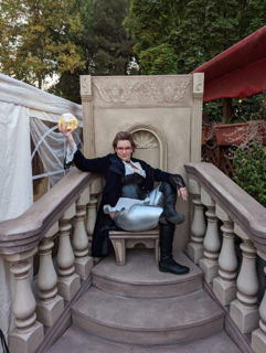 A woman in costume holds a crystal ball and sits on a throne