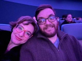 A man and a woman smile in a purple room