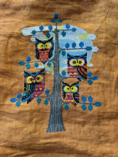 Three owls on a tree cross-stitched on orange fabric