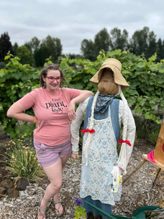 A woman poses with a scarecrow in a garden