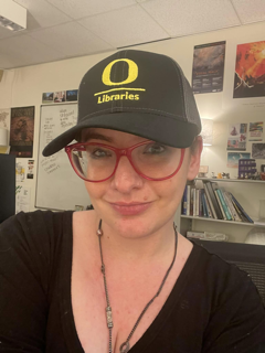 A woman in glasses and a baseball cap looks at the camera
